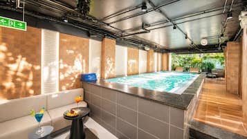 Un área de spa con un jacuzzi, una pequeña mesa con bebidas y fruta, y una piscina.