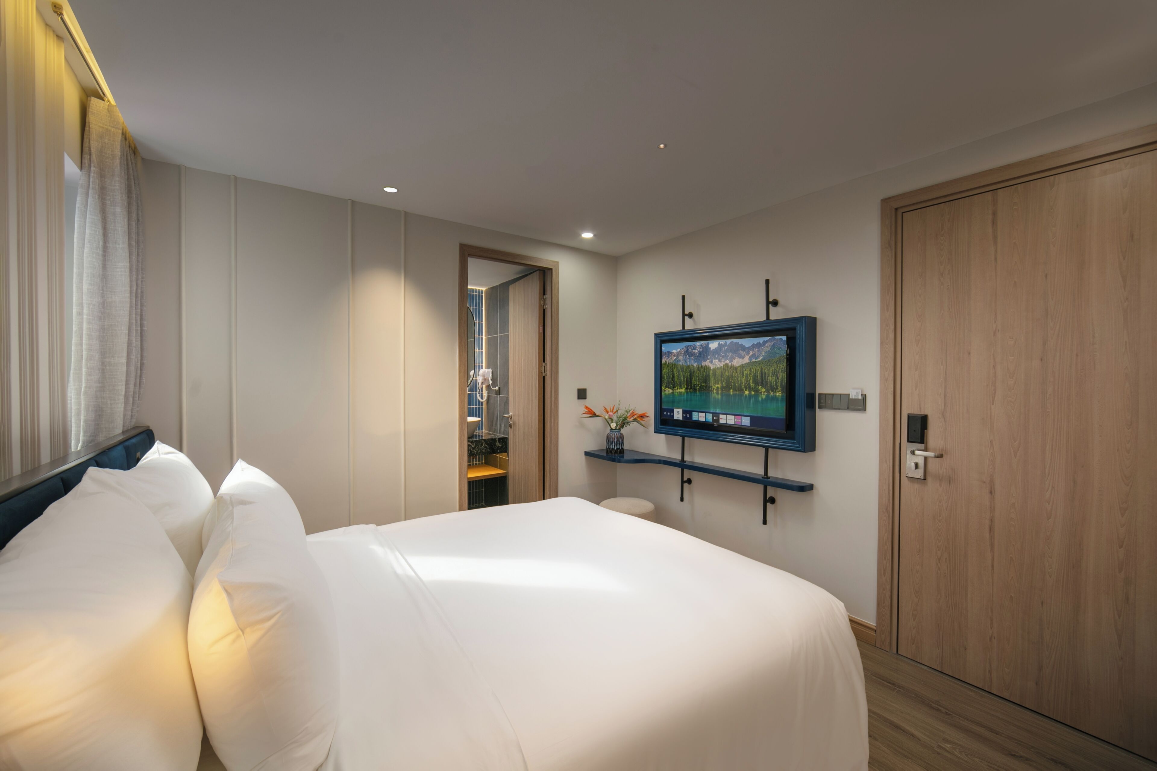 A hotel room with a bed, a television mounted on the wall, and a wooden door.