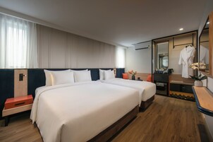 Habitación de hotel con dos camas, suelo de madera, un espejo, una bata y una mesita con un florero.