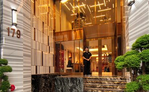 Fachada de hotel de mármol, con mostrador de recepción y una escalera que conduce al interior.