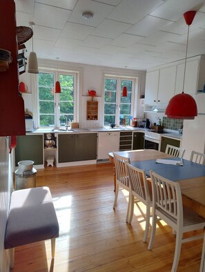 A kitchen with wooden flooring, white cabinets, a dining table with chairs, and a red pendant light. - Bornholm – Lovely apartment with sea view (Hollændergårde)