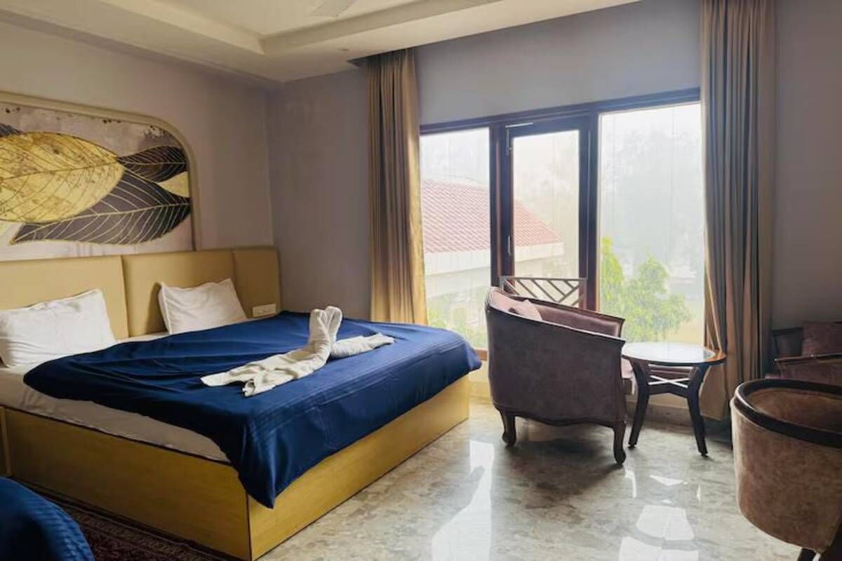 A hotel room with a bed, a chair, a small table, and a large window.