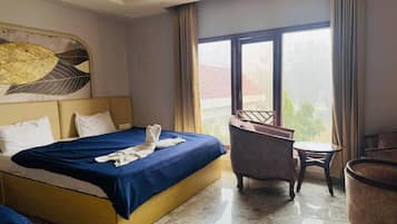 A hotel room with a bed, a chair, a small table, and a large window.