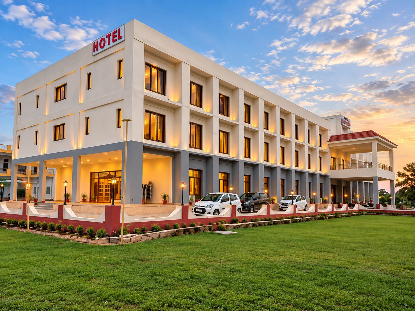 A hotel with a modern facade, multiple entry points, and a parking area with several cars.
