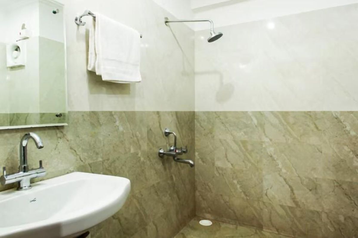 A bathroom with a sink, mirror, towel rack, shower, and marble walls.