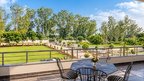 A terrace with a view of a well-maintained lawn and trees, a table with chairs, and a decorative vase. - Geetanjali hotel&motel (Bharatpur)