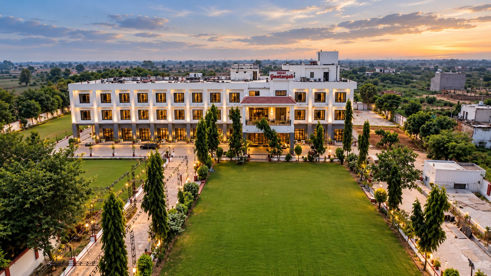 Un hotel de varios pisos con un patio central, rodeado de vegetación y un cielo despejado.