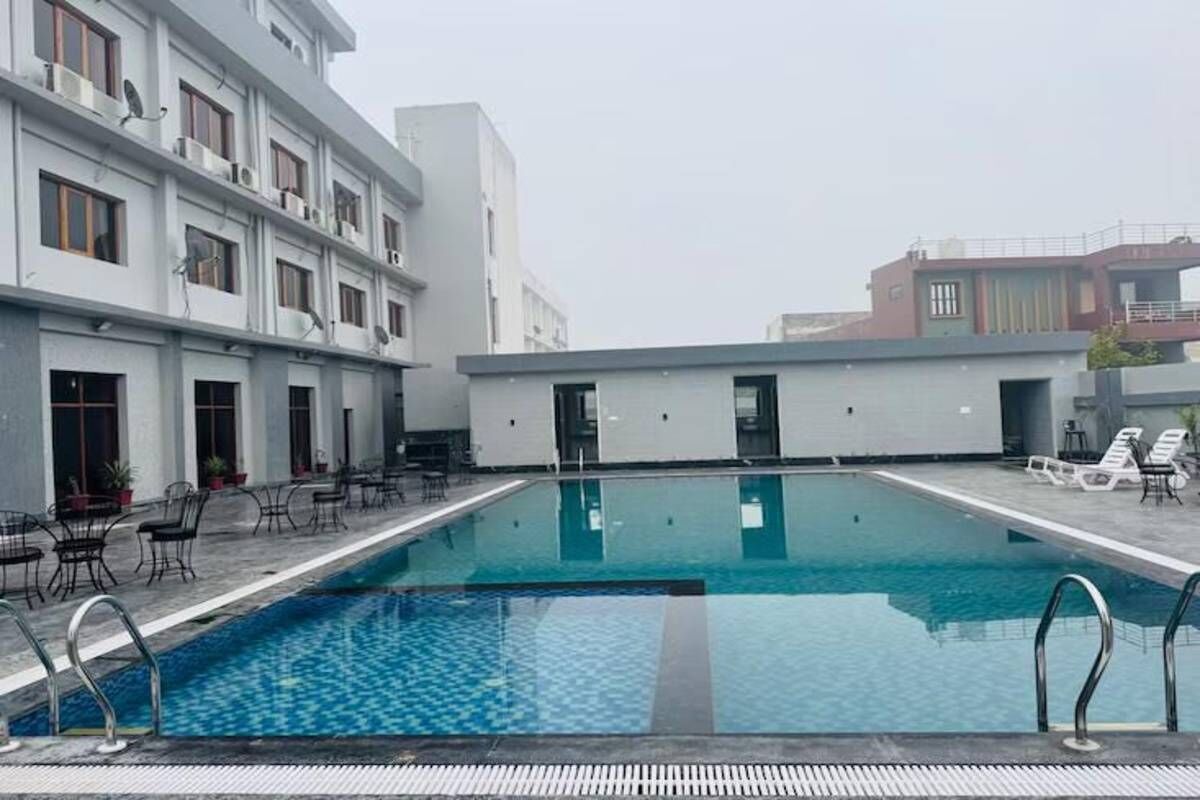 A rooftop swimming pool with lounge chairs and tables, surrounded by modern buildings.