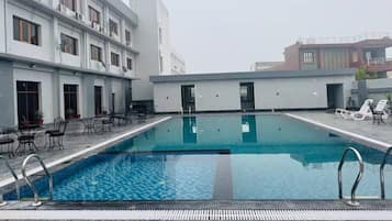 A rooftop swimming pool with lounge chairs and tables, surrounded by modern buildings.