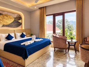 A hotel room with a large bed, a sitting area with a chair and a small table, and a view of the outdoors. - Geetanjali hotel&motel (Bharatpur)