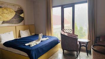 A hotel room with a bed, a chair, a small table, and a large window.