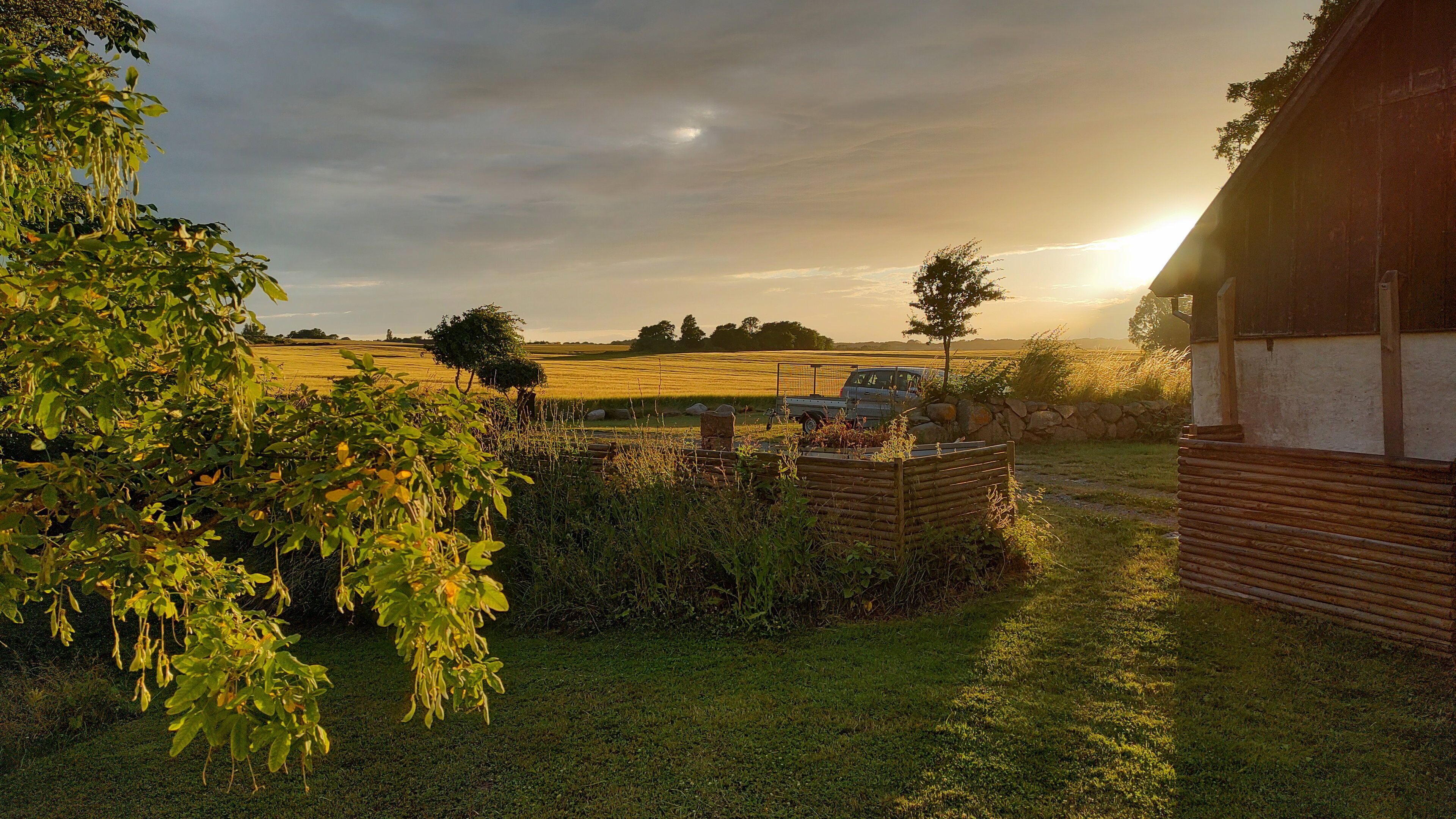 A rural landscape with a field, a wooden fence, and a building with a sloped roof.