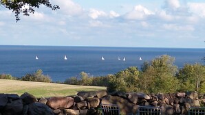En stenmur med stolar placerade så att man kan njuta av utsikten över havet och segelbåtarna.