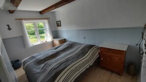 A bedroom with a bed, a wooden cabinet, a window with curtains, and a view of greenery outside. - Lovely holiday apartment on Bornholm (Hollændergårde)