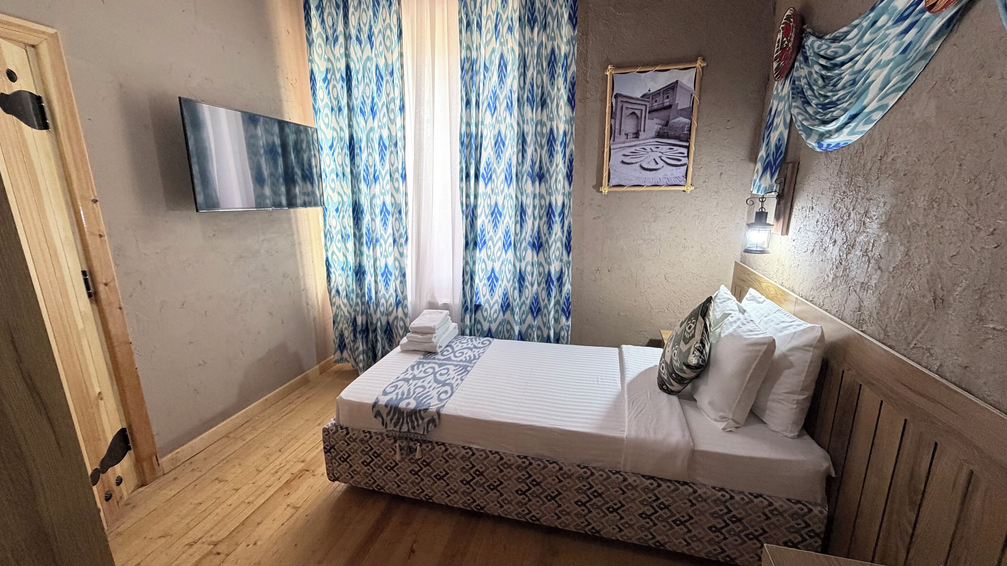 Ein Schlafzimmer mit Bett, Vorhängen, einem an der Wand befestigten Fernseher und einem Wandbild.
