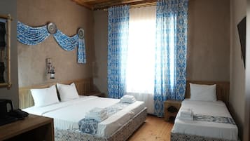 A room with two beds, wooden flooring, a ceiling fan, and patterned curtains.