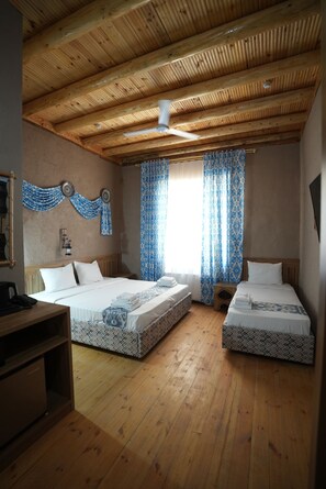 Une chambre avec deux lits, un plancher en bois, un ventilateur de plafond et des rideaux à motifs.