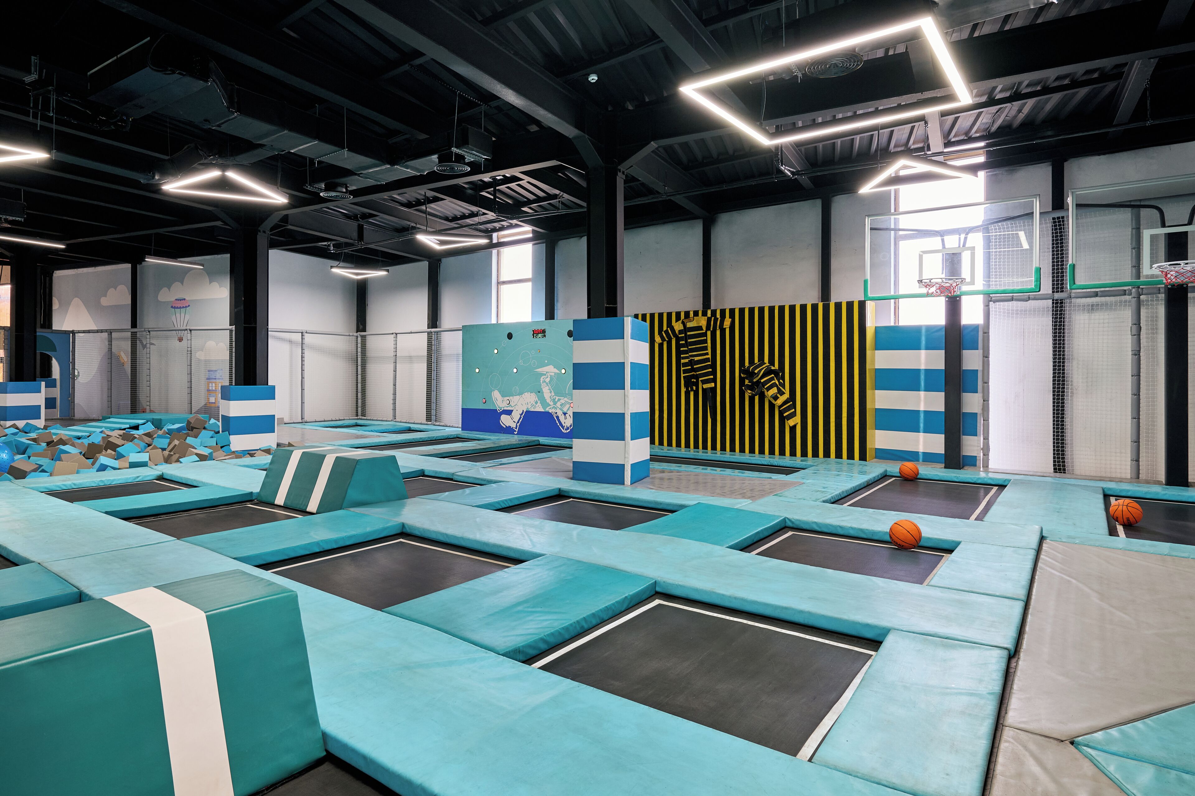 Parque de trampolines cubierto con múltiples trampolines, paredes acolchadas y un aro de baloncesto.