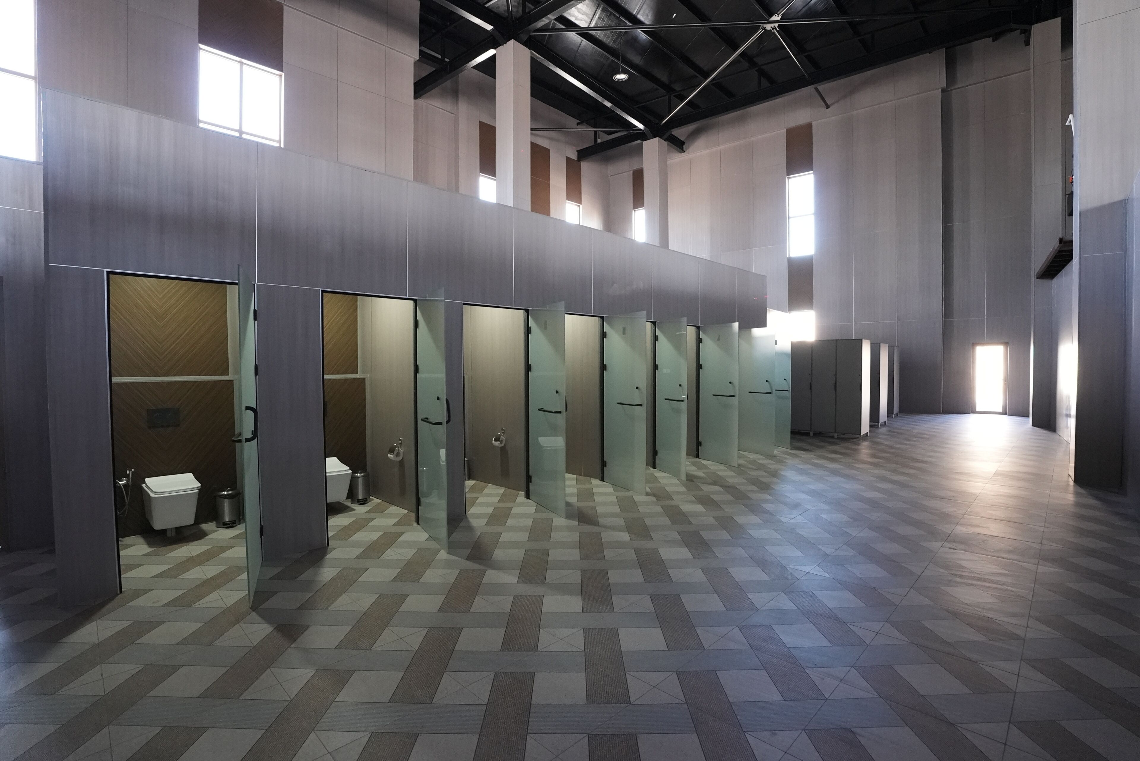 Een moderne toiletruimte met glazen scheidingswanden, een geruit vloertje en een hoge plafond.