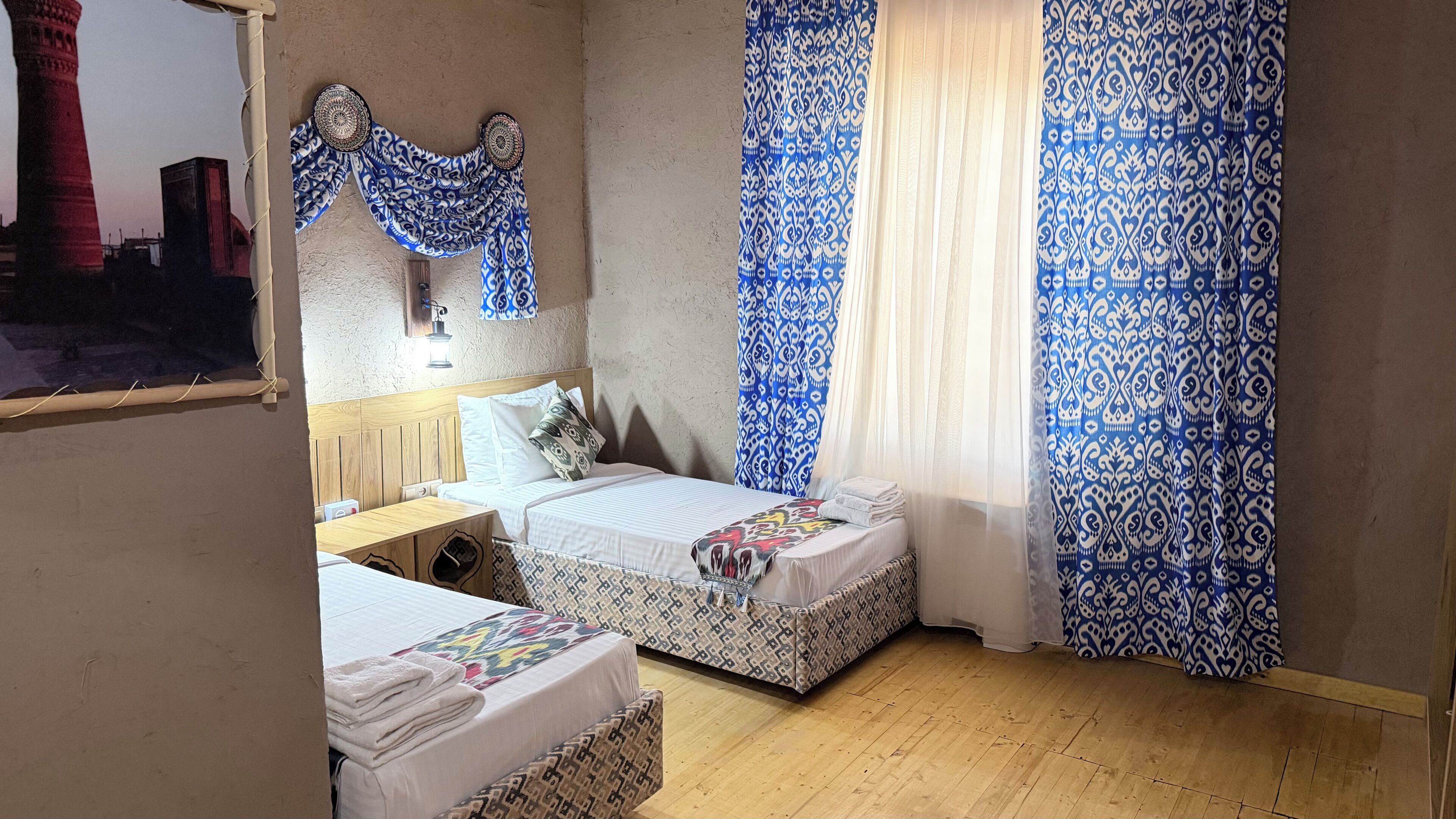 Una habitación con dos camas, cabecero de madera, cortinas estampadas y suelo de madera.