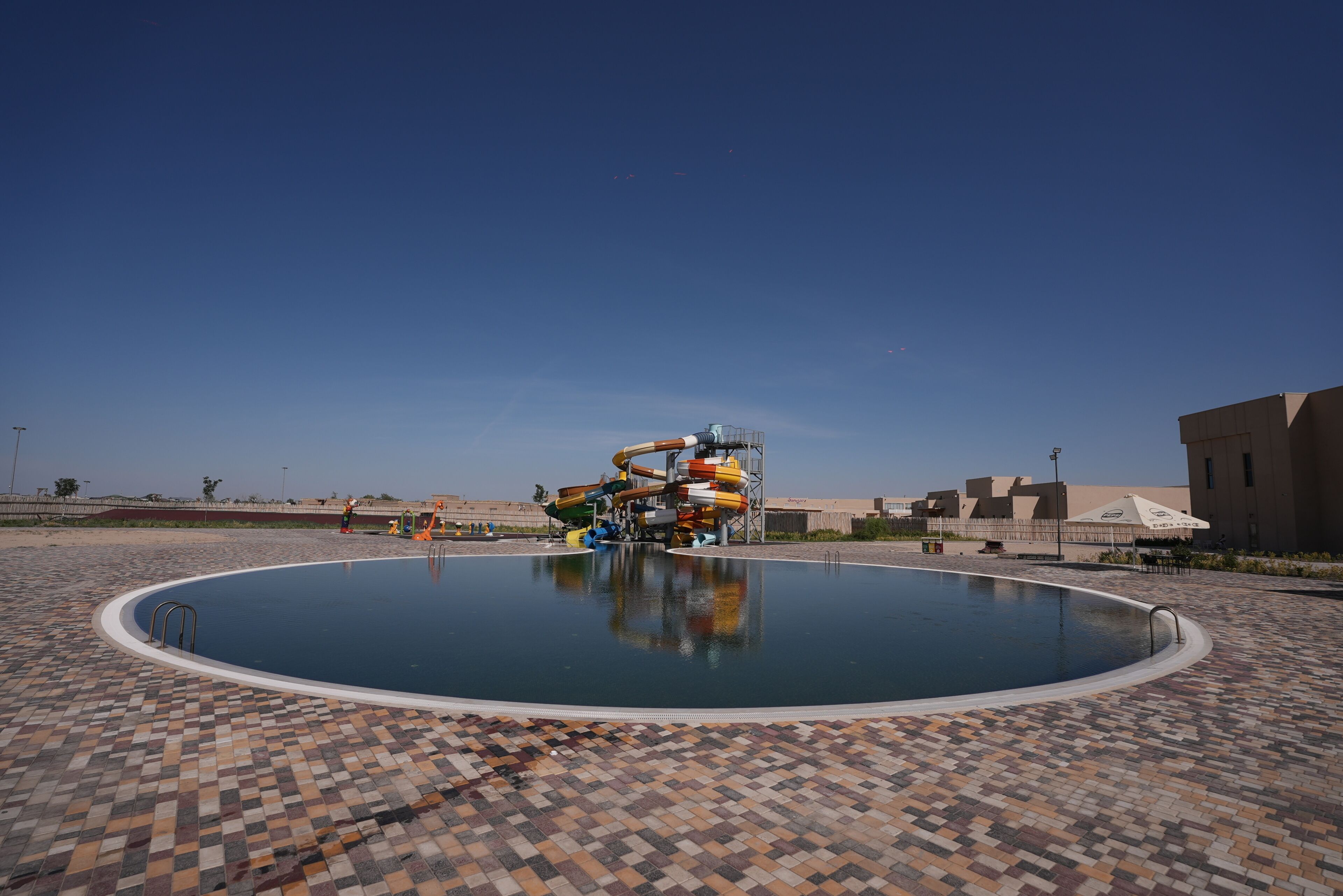 Ein Swimmingpool mit Wasserrutsche, einer gefliesten Liegefläche und blauem Himmel.