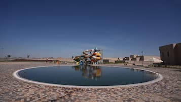 Ein Swimmingpool mit Wasserrutsche, einer gefliesten Liegefläche und blauem Himmel.