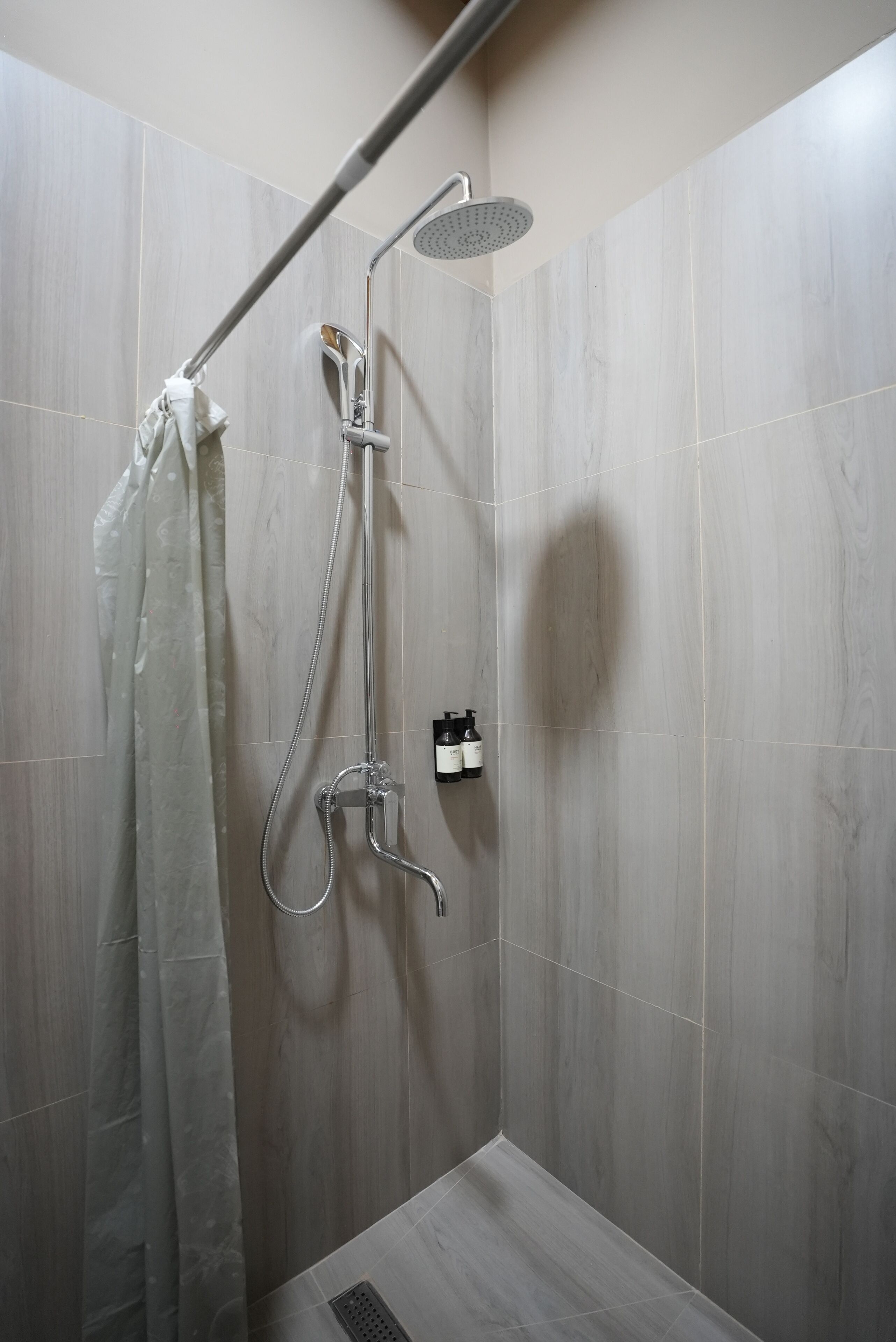 A shower with a handheld showerhead and a wall-mounted rain showerhead, a towel rack, and a small shelf with toiletries.