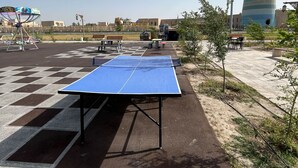Ett bordtennisbord på en utomhusplats med bänkar, ett staket och byggnader i bakgrunden.