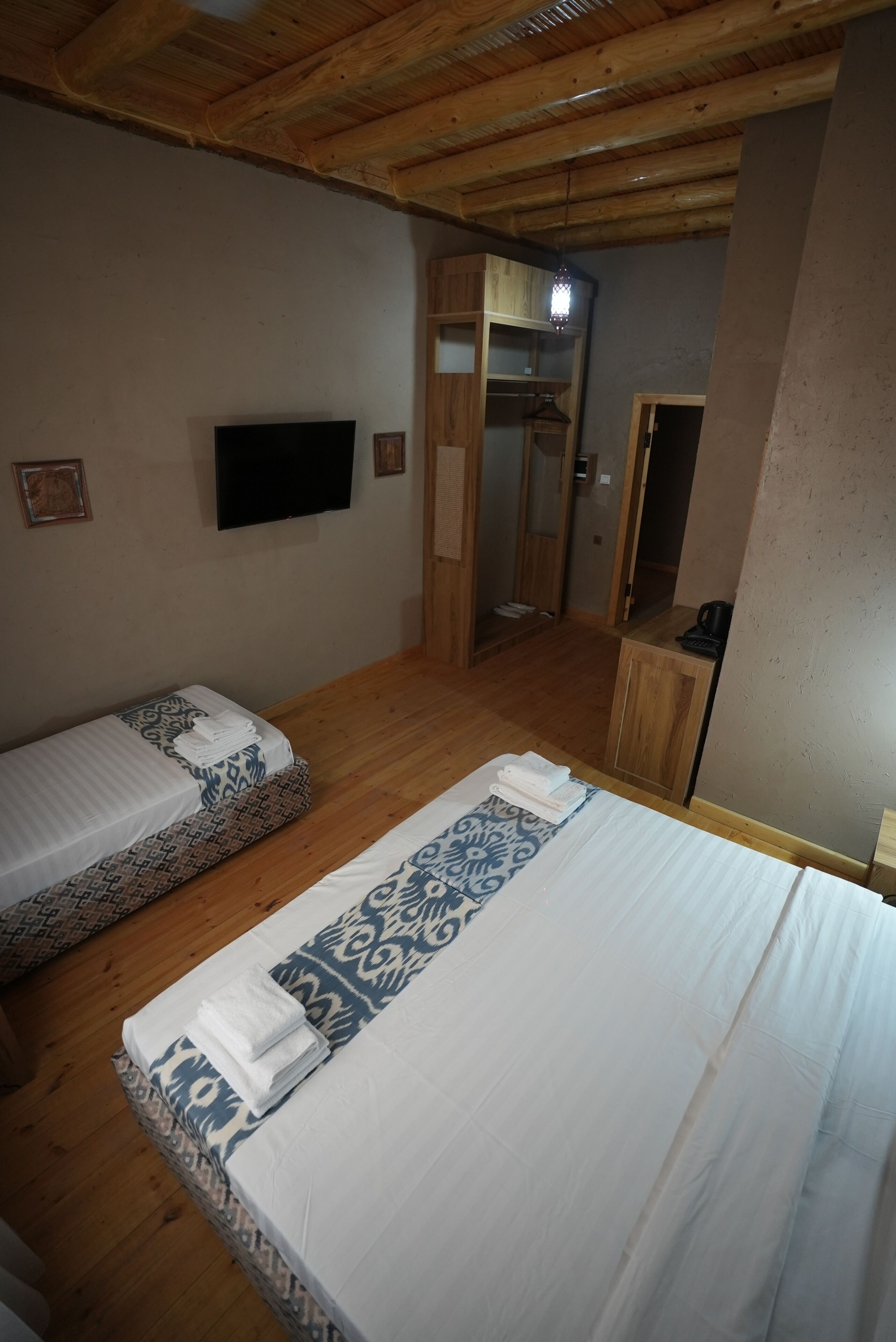 Een kamer met twee bedden, een televisie en een houten plafond.