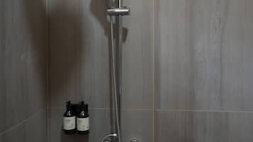 A shower with a handheld showerhead and a wall-mounted faucet. There are two bottles of shampoo and conditioner on the wall.