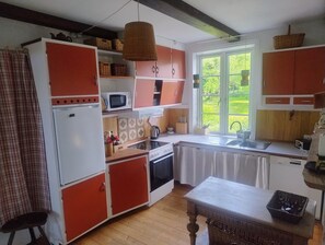 Eine Küche mit roten Schränken, einem weißen Kühlschrank, einer Mikrowelle, einem Herd und einem Fenster mit Blick auf Grünflächen.