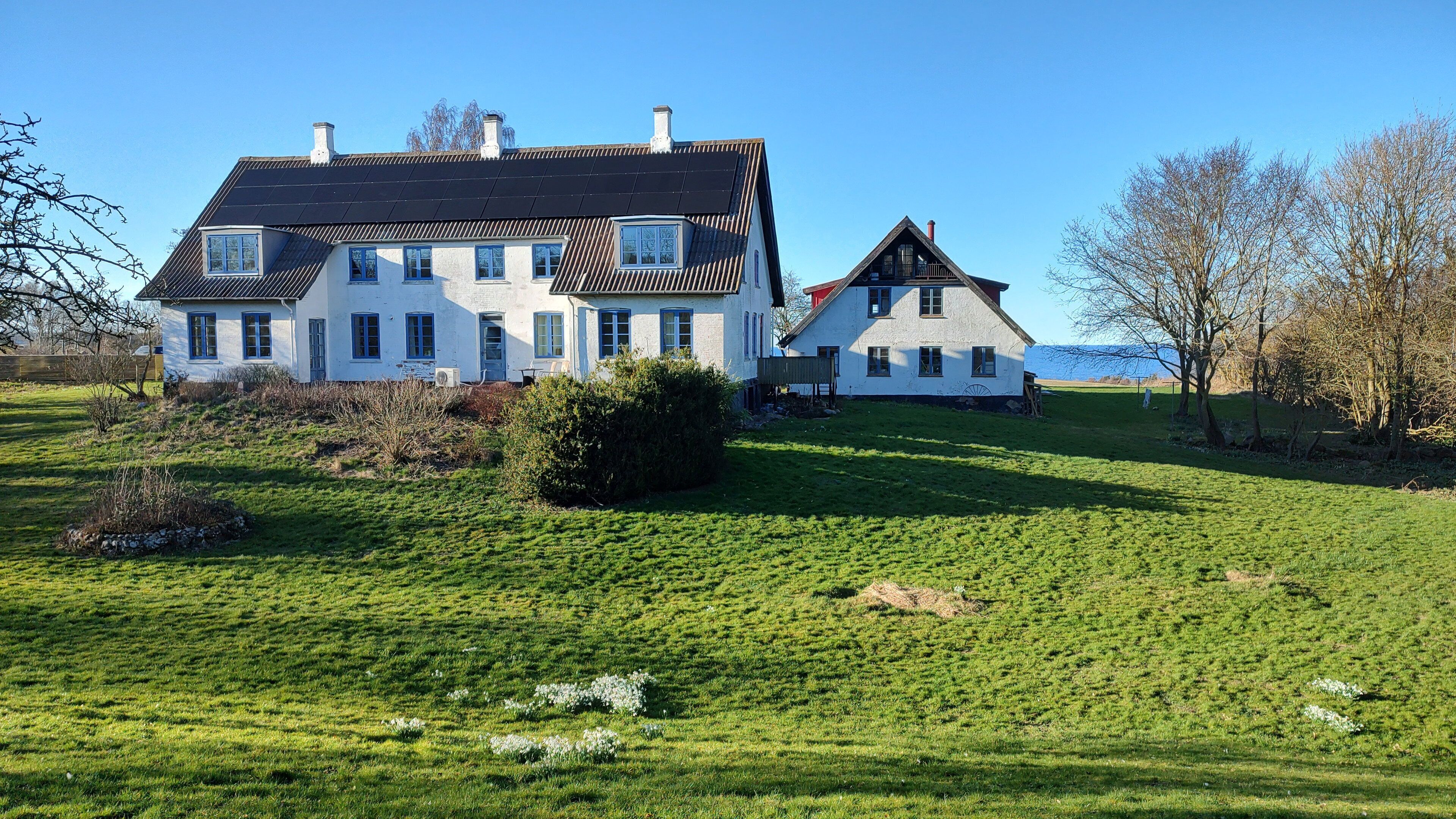 A large white house with multiple windows and a sloped roof, surrounded by a grassy field and trees.