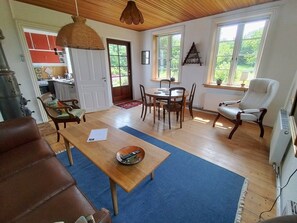A spacious living room with a wooden dining table, a leather sofa, and a large window providing natural light.