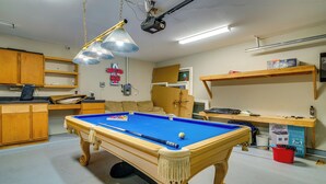 Een pooltafel in een ruimte met houten kasten, een plafondprojector en een neonbord.