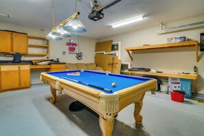 Ein Billardtisch in einem Raum mit Holzausbau, einem an der Decke befestigten Projektor und einer Neonreklame.