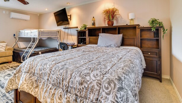 Een slaapkamer met een stapelbed, een bureau, een televisie, een kamerplant en een bed met een gestreept beddegoed.
