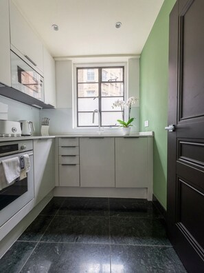 A compact kitchen with a window, a stove, and a sink. - Prime 2 bedrooms flat in Knightsbridge- Harrods view / portable air conditioning (London)