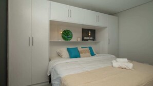Une chambre à coucher avec un lit, une armoire blanche et une étagère ornée d’objets décoratifs.