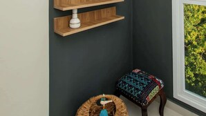 Une pièce d  ’angle avec un mur foncé, deux miroirs ronds, des étagères en bois, une plante en pot, un tabouret en osier et un banc avec un coussin à motifs.