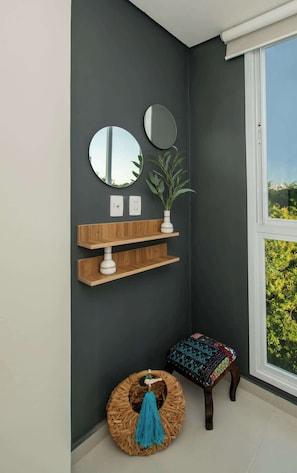 A corner room with a dark wall, two round mirrors, wooden shelves, a potted plant, a wicker stool, and a bench with a patterned cushion. - Corporate Stays First Living - 206 (Asunción)