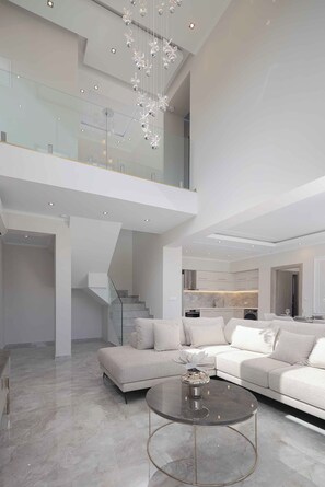 A modern interior with a high ceiling, a glass railing, a staircase, a living area with a sofa, and a dining area. - Atriora Luxury Villa | Private Pool & 150m to sea! (Kissamos)