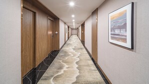Un pasillo de hotel con puertas de madera, alfombra estampada y un cuadro en la pared.