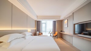 Habitación de hotel con una cama grande, televisión, una mesita con una silla y vistas a la ciudad desde la ventana.