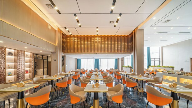 Un amplio comedor de hotel con varias mesas y sillas, piso de mármol y un diseño moderno en el techo.