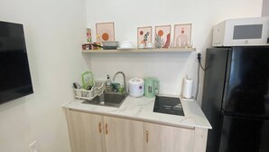 Eine kleine Küche mit Spüle, Mikrowelle, Kühlschrank und einer Arbeitsplatte mit verschiedenen Küchenutensilien.