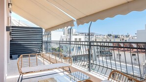 Ein Balkon mit Korbmöbeln, einem Glastisch und Blick auf die Stadt.