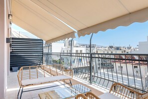 A balcony with wicker furniture, a glass table, and a view of the cityscape. - Skyline Penthouse (Athina)