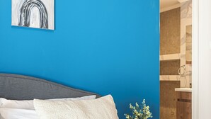 Ein Schlafzimmer mit einem Bett, Kissen, einem Nachttisch, einer Vase mit Blumen und einer blauen Wand.