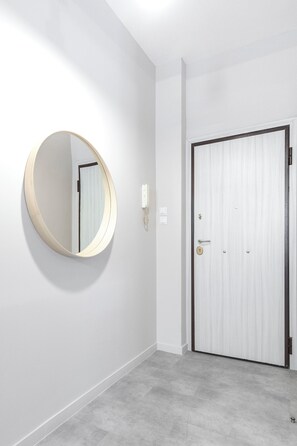 A hallway with a round mirror on the wall, a door with a doorknob, and a light switch. - Skyline Penthouse (Athina)