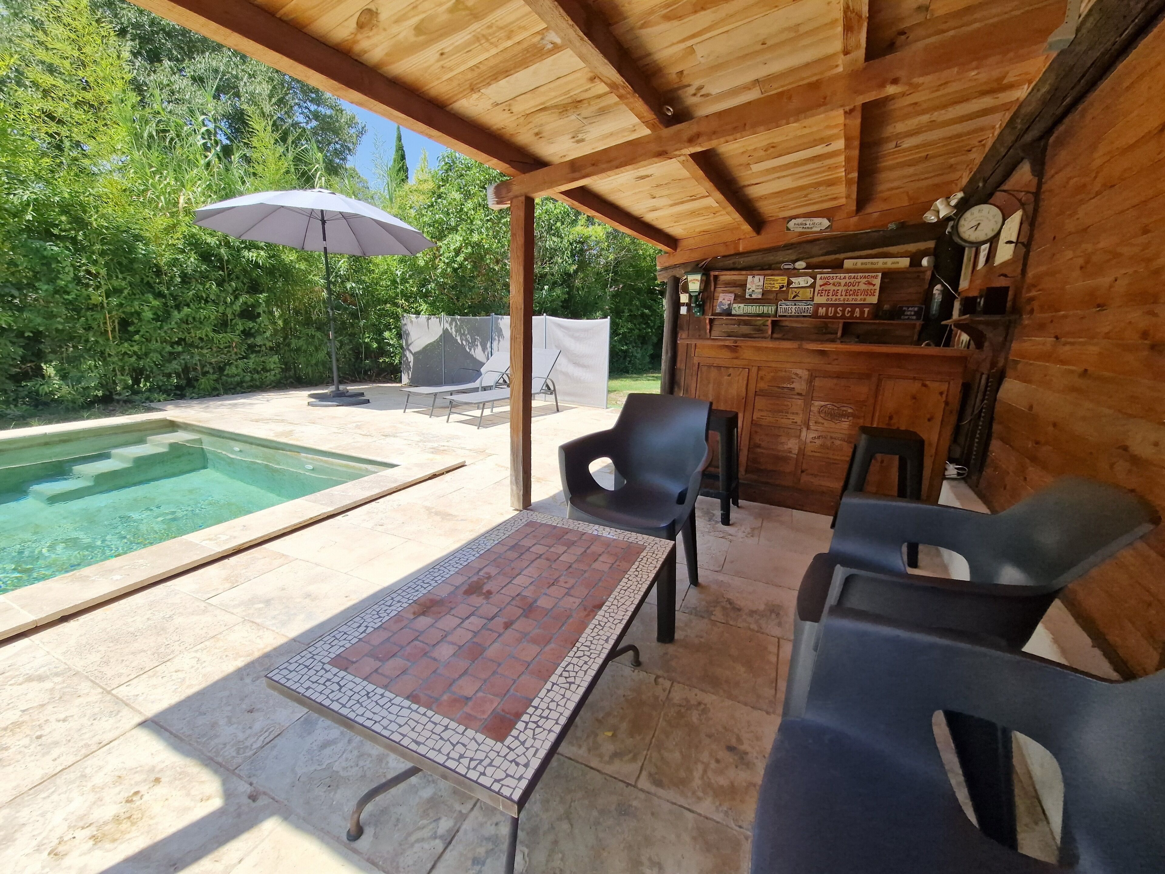 A covered outdoor area with a pool, lounge chairs, and a bar.